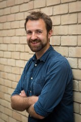 author standing against a wall with his hands folded over his chest